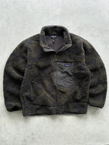 A Patagonia fleece jacket in a dark brown and black textured pattern, laid flat on a light gray concrete surface.