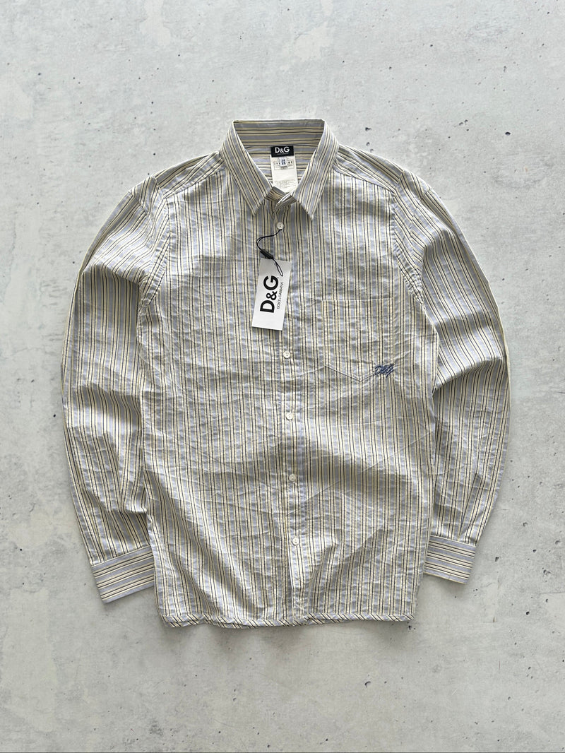 A D&G long-sleeve button-up shirt in a beige and white textured stripe pattern, laid flat on a light gray concrete surface with a paper tag still attached.