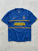 A blue Juventus soccer jersey with yellow accents, featuring the New York/New Jersey club crest and a New Holland sponsor logo, laid flat on a gray concrete surface.