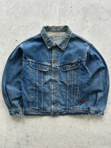 A classic blue Valentino vintage denim jacket with a button-up front, chest flap pockets, and side slip pockets, laid flat on a textured gray concrete surface.